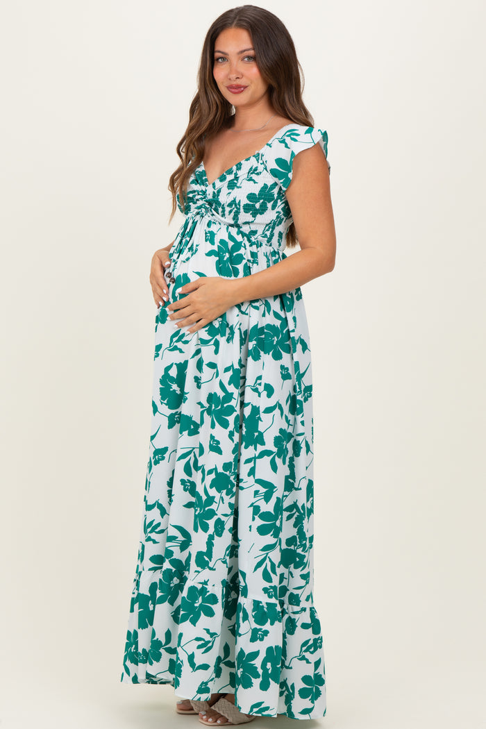 woman wearing a green and white floral print maternity maxi dress and holding her baby bump