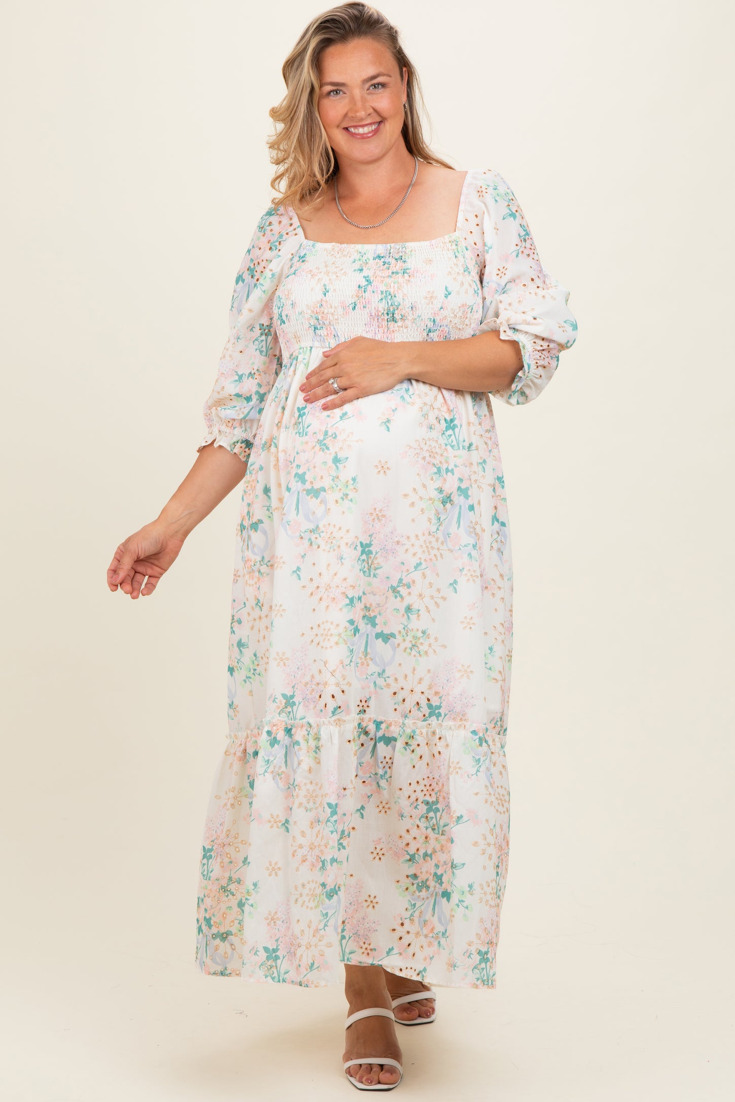 woman wearing a floral print maternity plus maxi dress with smocked bodice and long sleeves, showing her baby bump