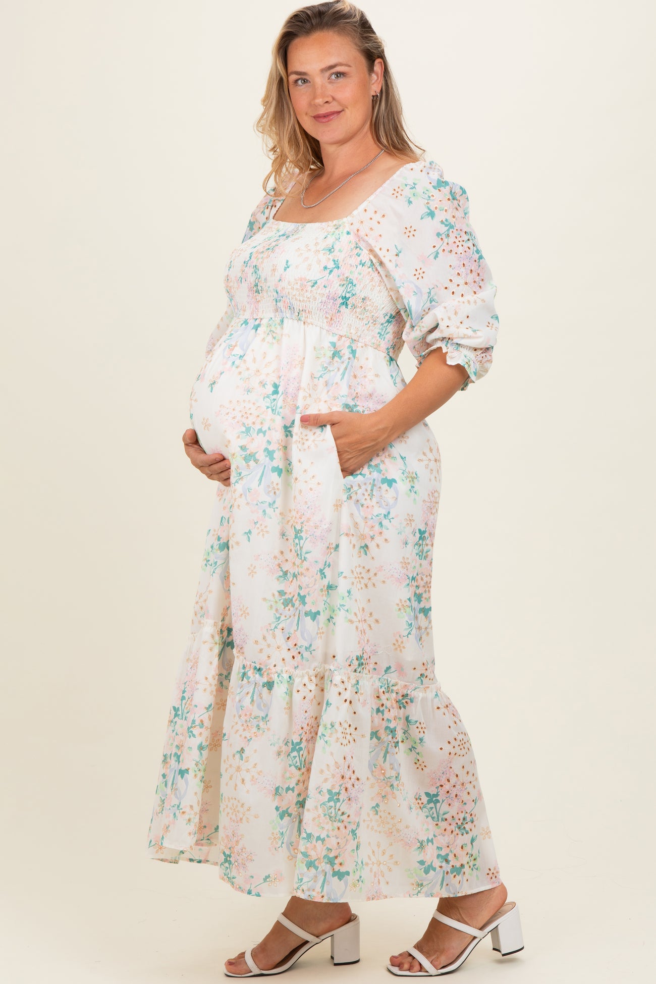 woman wearing a floral maternity dress with puff sleeves and a tiered hem, showing her baby bump and posing with one hand on her belly