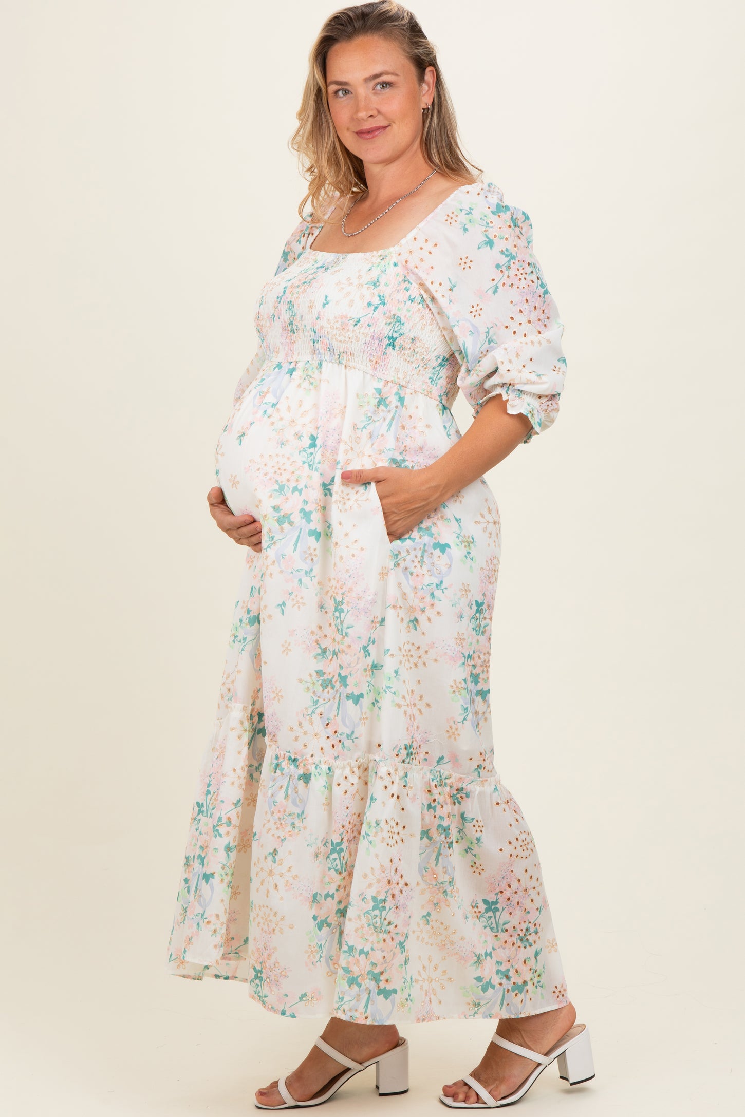 woman wearing a floral maternity dress with puff sleeves and a tiered hem, showing her baby bump and posing with one hand on her belly