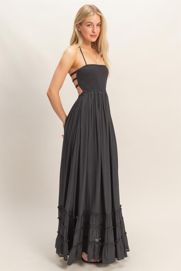 woman wearing a black maxi dress with a smocked bodice and ruffled hem, featuring back cutouts and adjustable straps