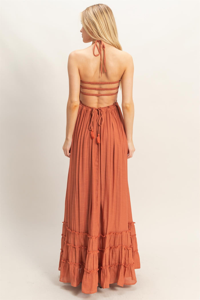 woman wearing a rust-colored maxi dress with a halter neck and tiered ruffle hem, showing a tied back design