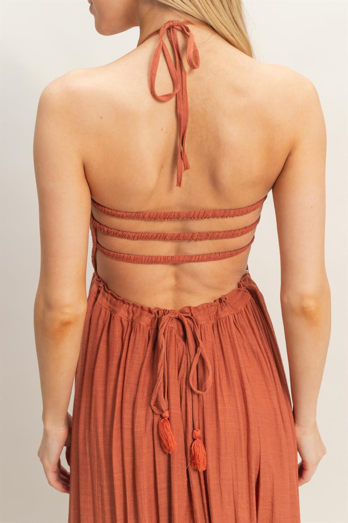 woman wearing an rust-colored halter neck dress with a strappy back and tassel ties