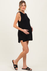 woman wearing a black sleeveless maternity top and showing her baby bump while posing in casual shorts.