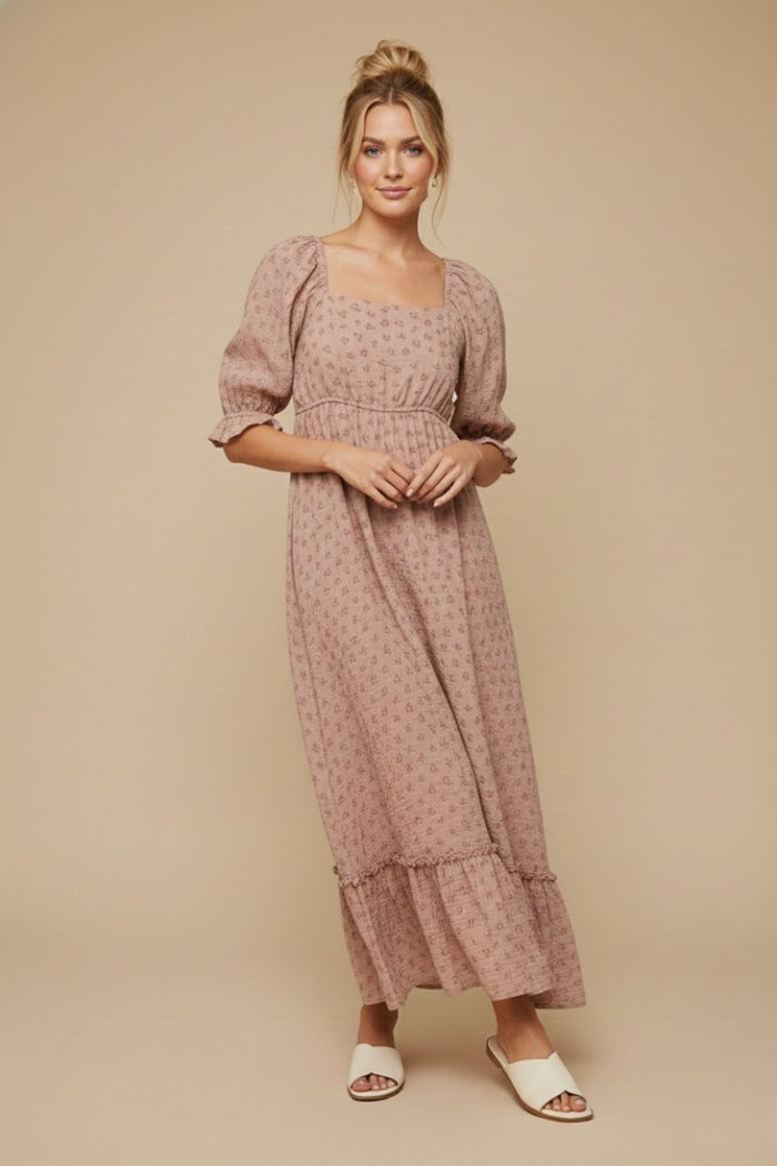 woman wearing a pink floral maxi dress with puff sleeves and ruffle hem, standing against a neutral background