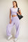 woman wearing a lavender cropped t-shirt and matching loose sweatpants, carrying a black bag, styled casually