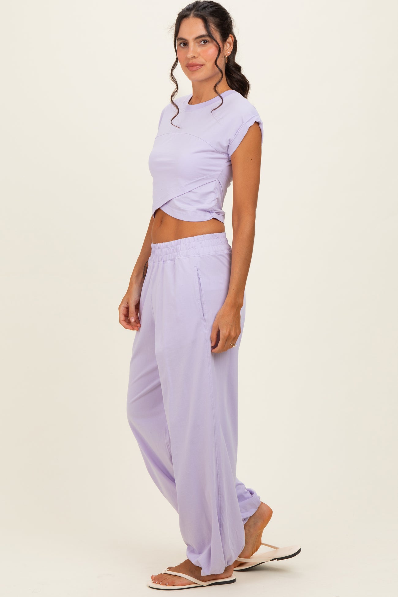 woman wearing a lavender cropped t-shirt and matching wide-leg pants, styled with flip-flops and loose waves in her hair