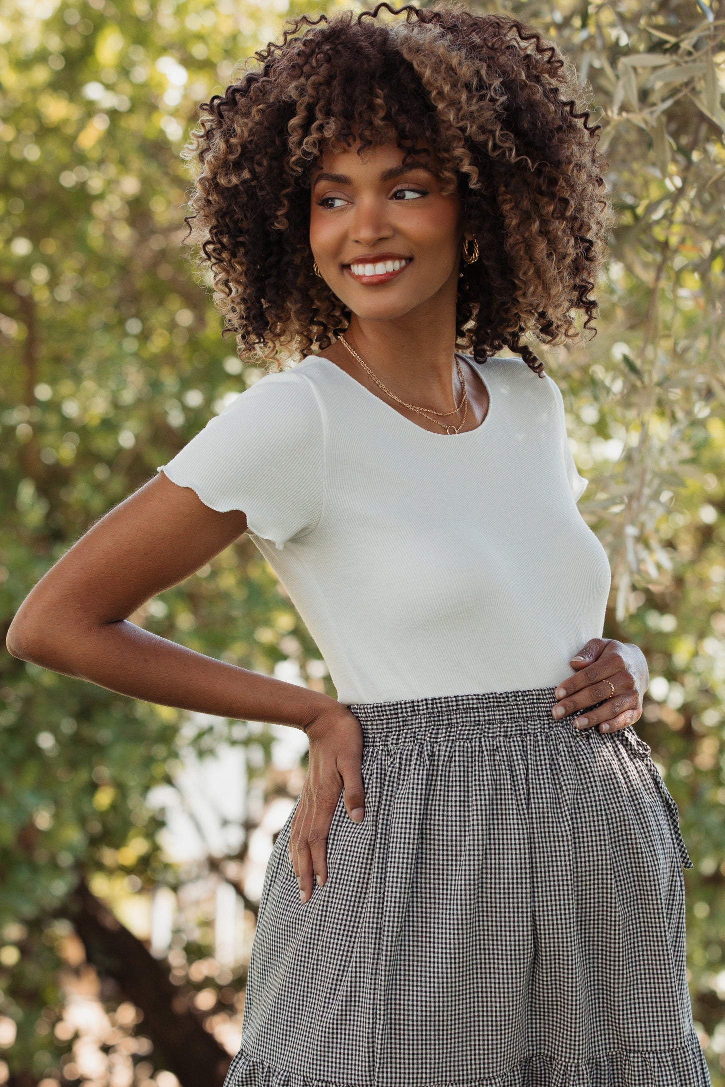 woman wearing a white short sleeve maternity top and a patterned skirt, highlighting her baby bump