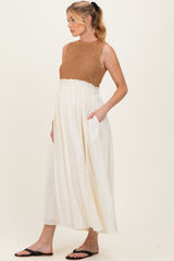woman wearing a brown crochet maternity top and a white maxi skirt with pockets, showing her baby bump