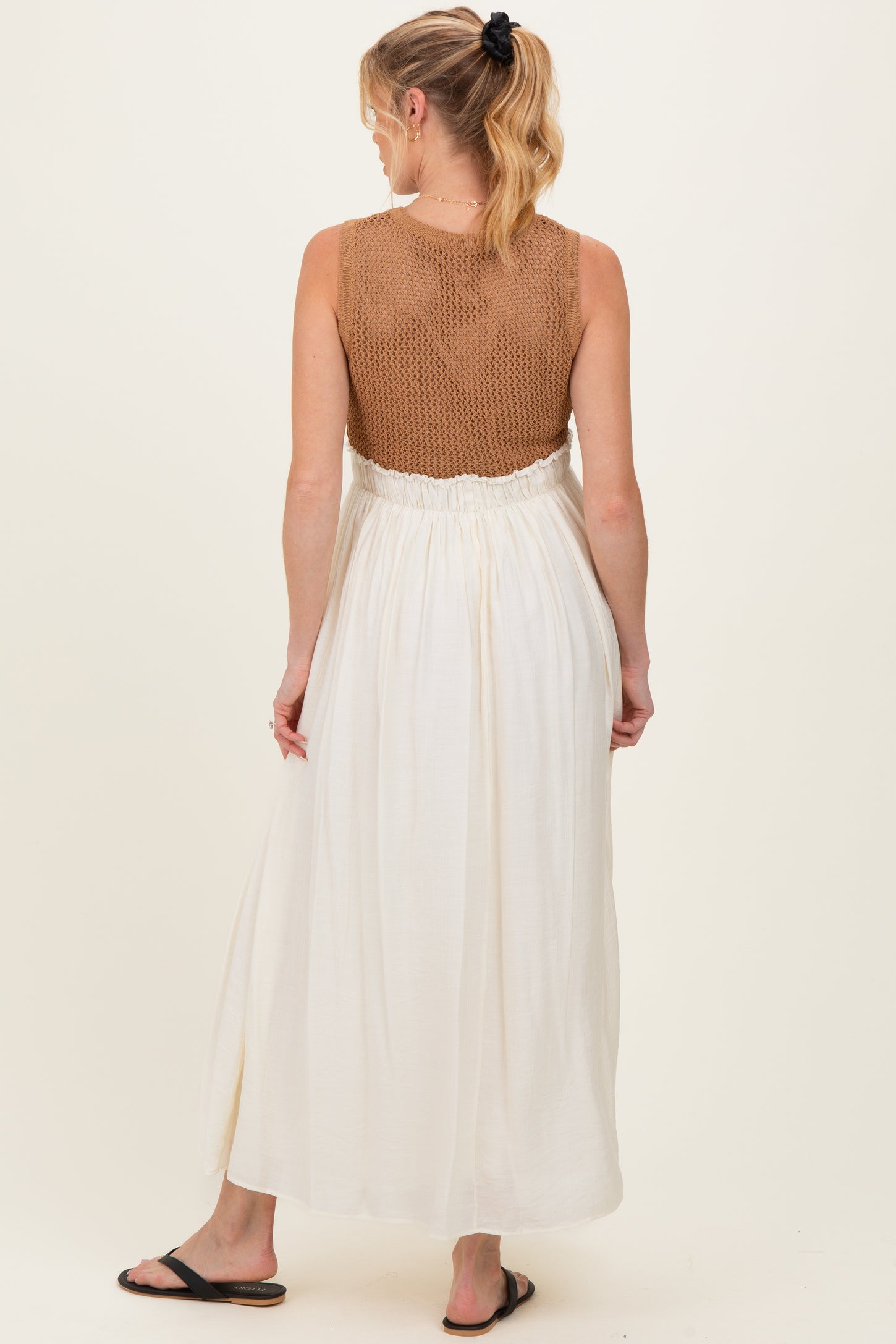 woman wearing a sleeveless maternity maxi dress with a crochet top and flowy white skirt, showing her back