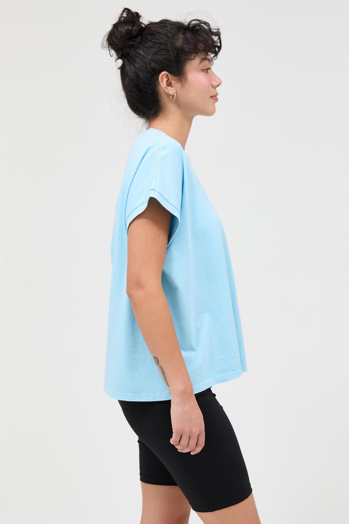 woman wearing a light blue oversized t-shirt and black bike shorts, standing in a side profile view