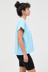 woman wearing a light blue oversized t-shirt and black bike shorts, standing in a side profile view