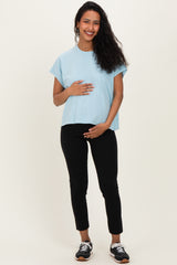 woman wearing a light blue maternity top and black maternity pants, holding her baby bump
