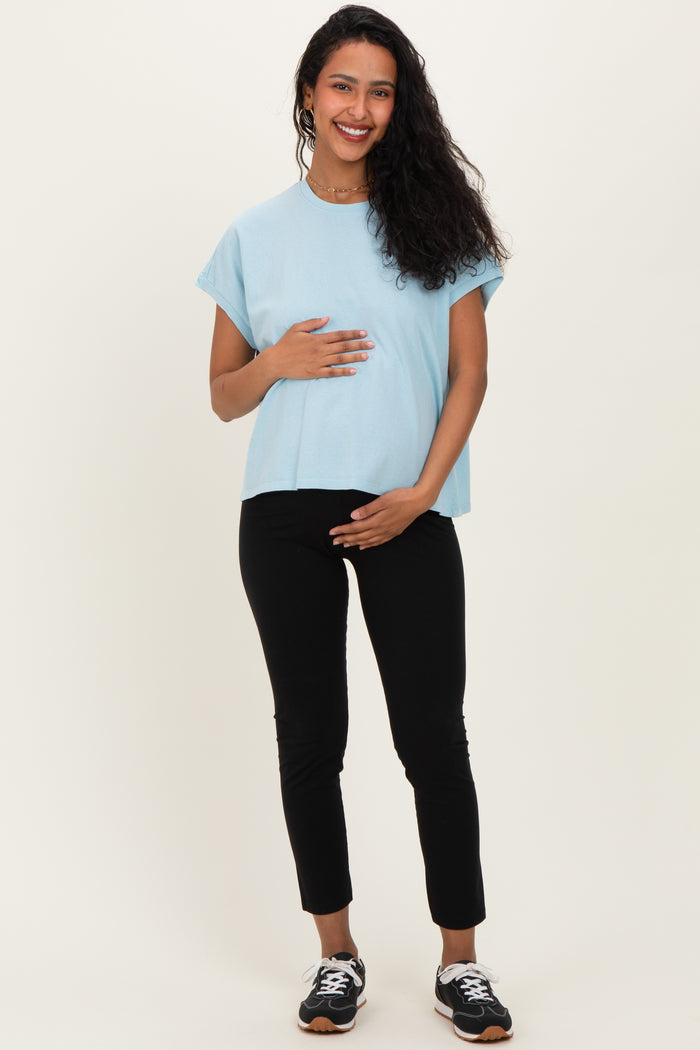 woman wearing a light blue maternity top and black maternity pants, holding her baby bump