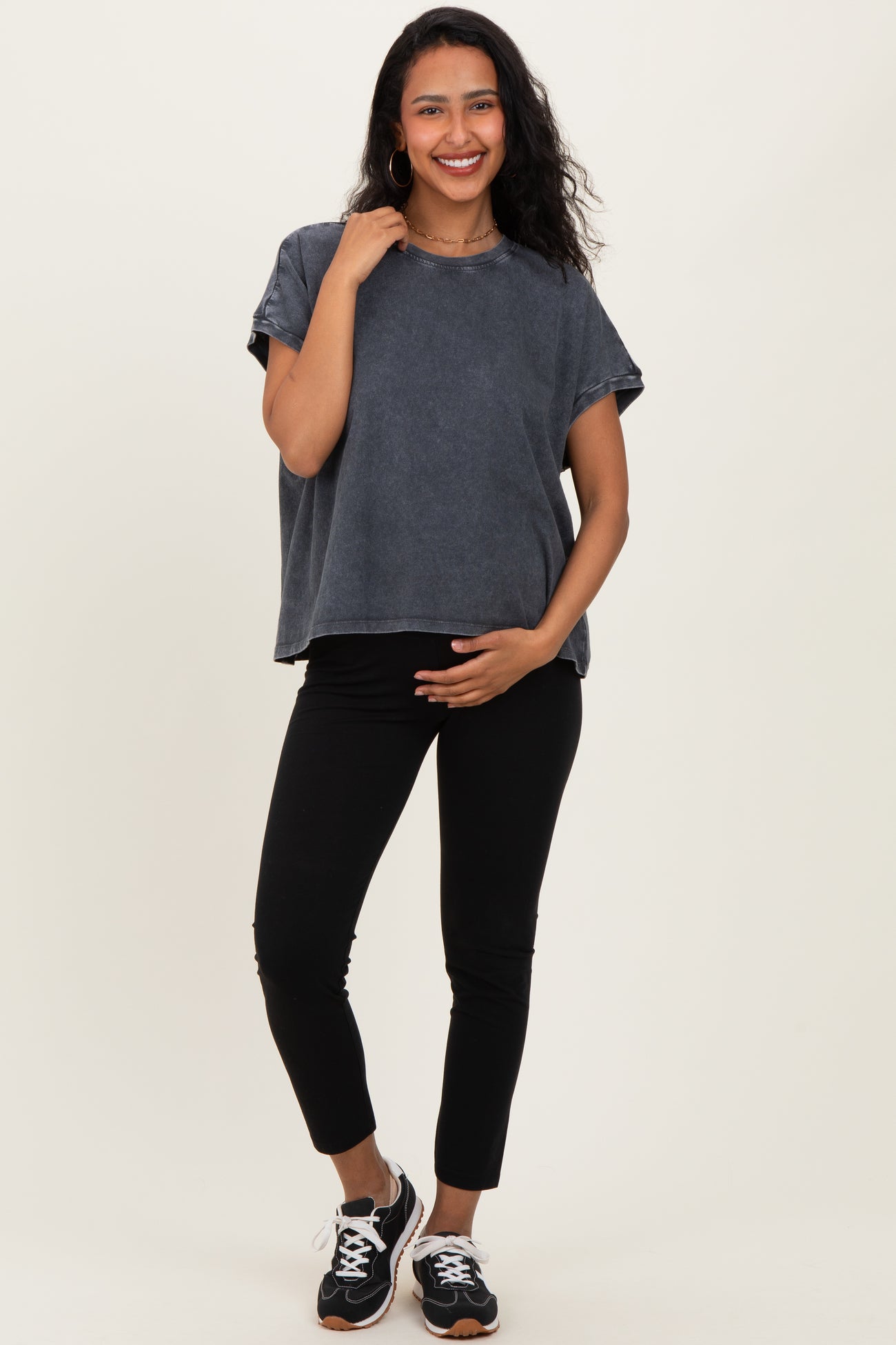 woman wearing a dark gray maternity top and black leggings, holding her baby bump