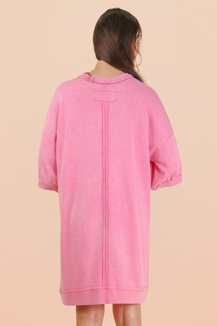 woman wearing a pink oversized hooded sweatshirt dress with short sleeves and a back seam detail