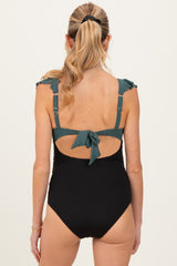 woman wearing a black ribbed one-piece maternity swimsuit with teal ruffled straps and a back tie detail