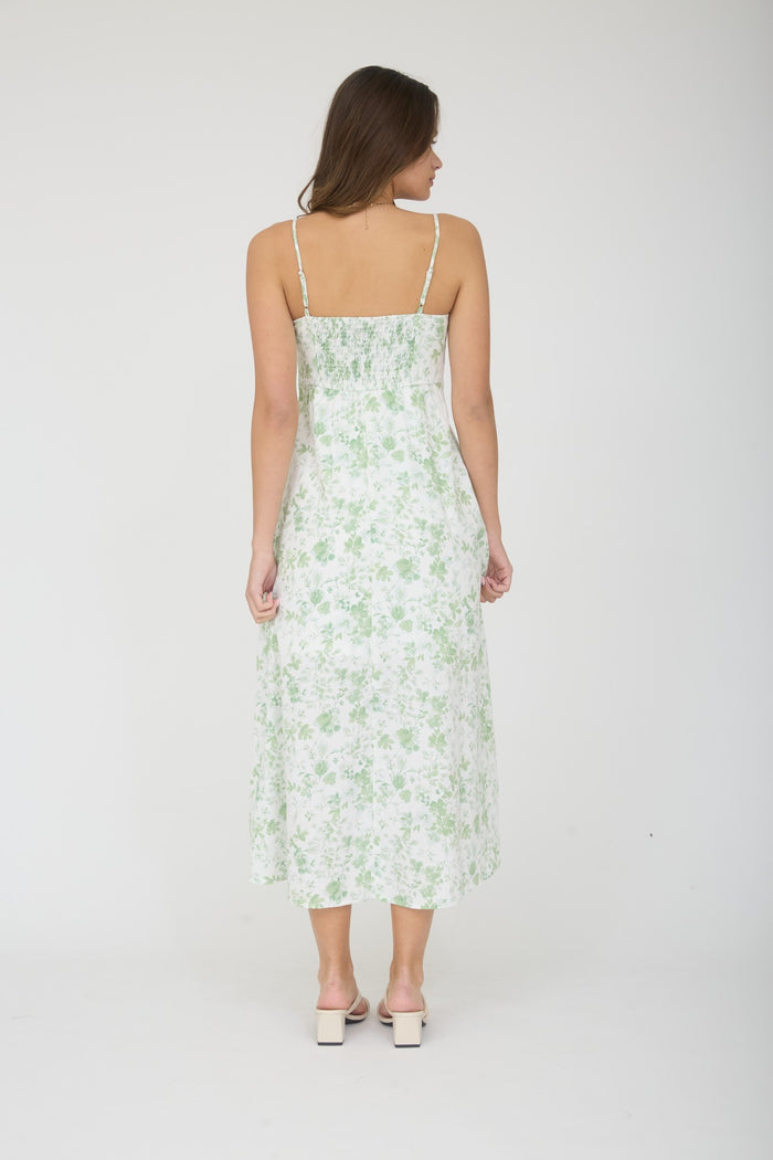 woman wearing a white floral midi dress with green patterns and spaghetti straps, shown from the back