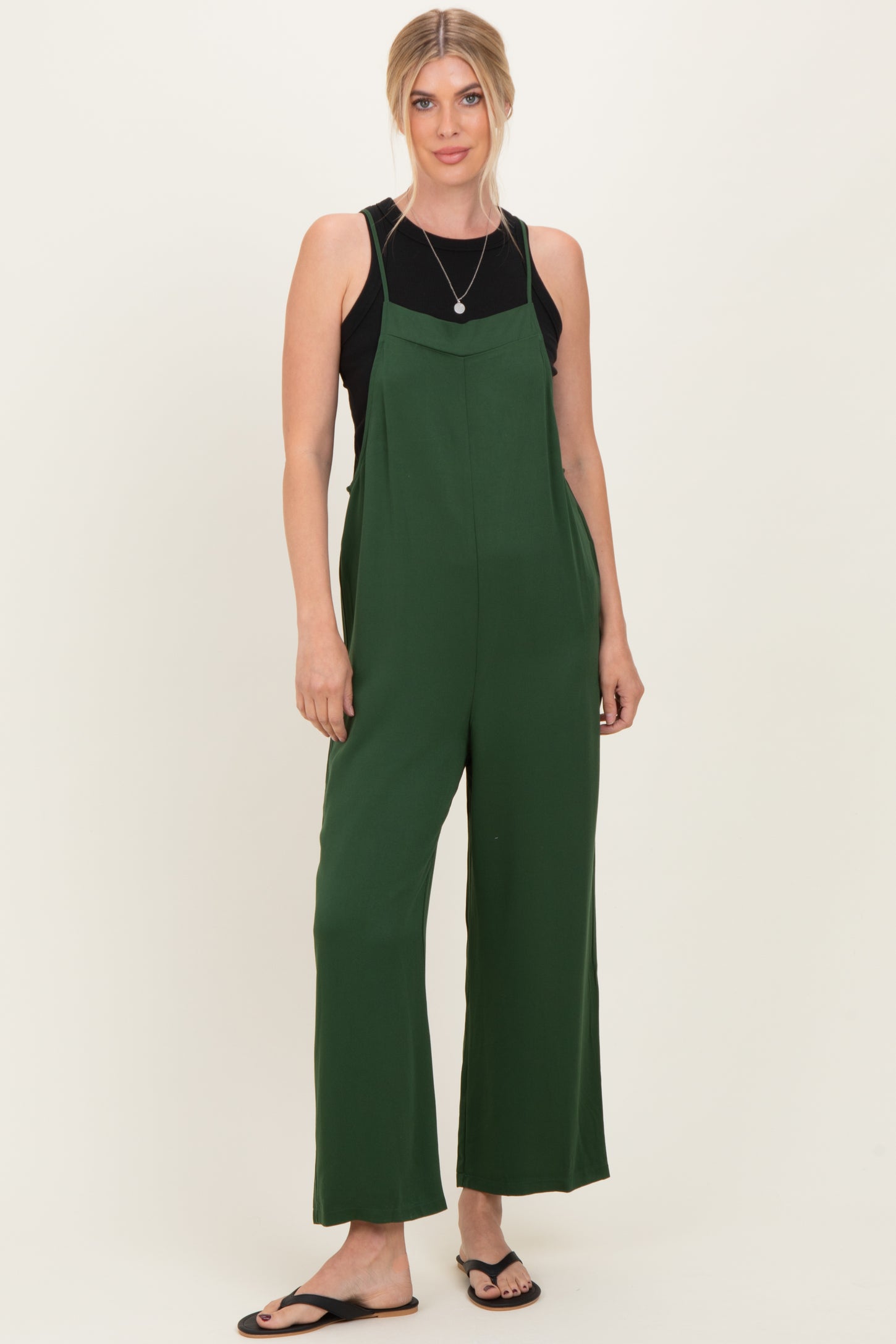 woman wearing a green wide-leg jumpsuit over a black tank top and flip flops