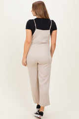 woman wearing a beige maternity jumpsuit with adjustable straps and a fitted silhouette, showing a pregnant belly from the back