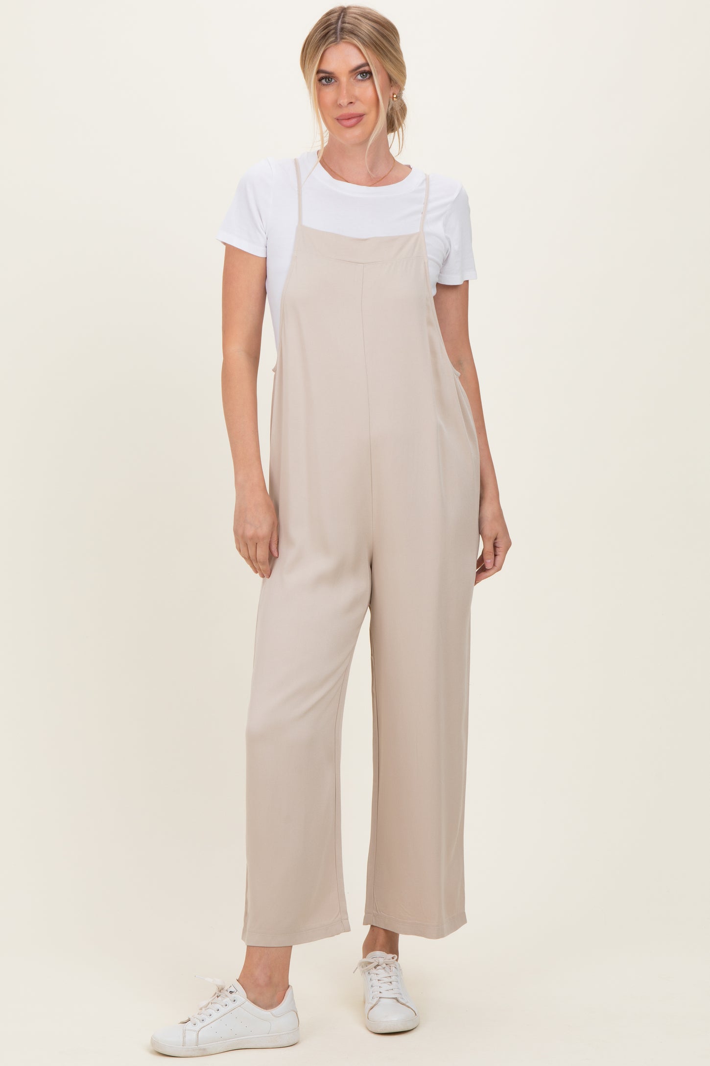 woman wearing a beige wide-leg jumpsuit over a white t-shirt with white sneakers