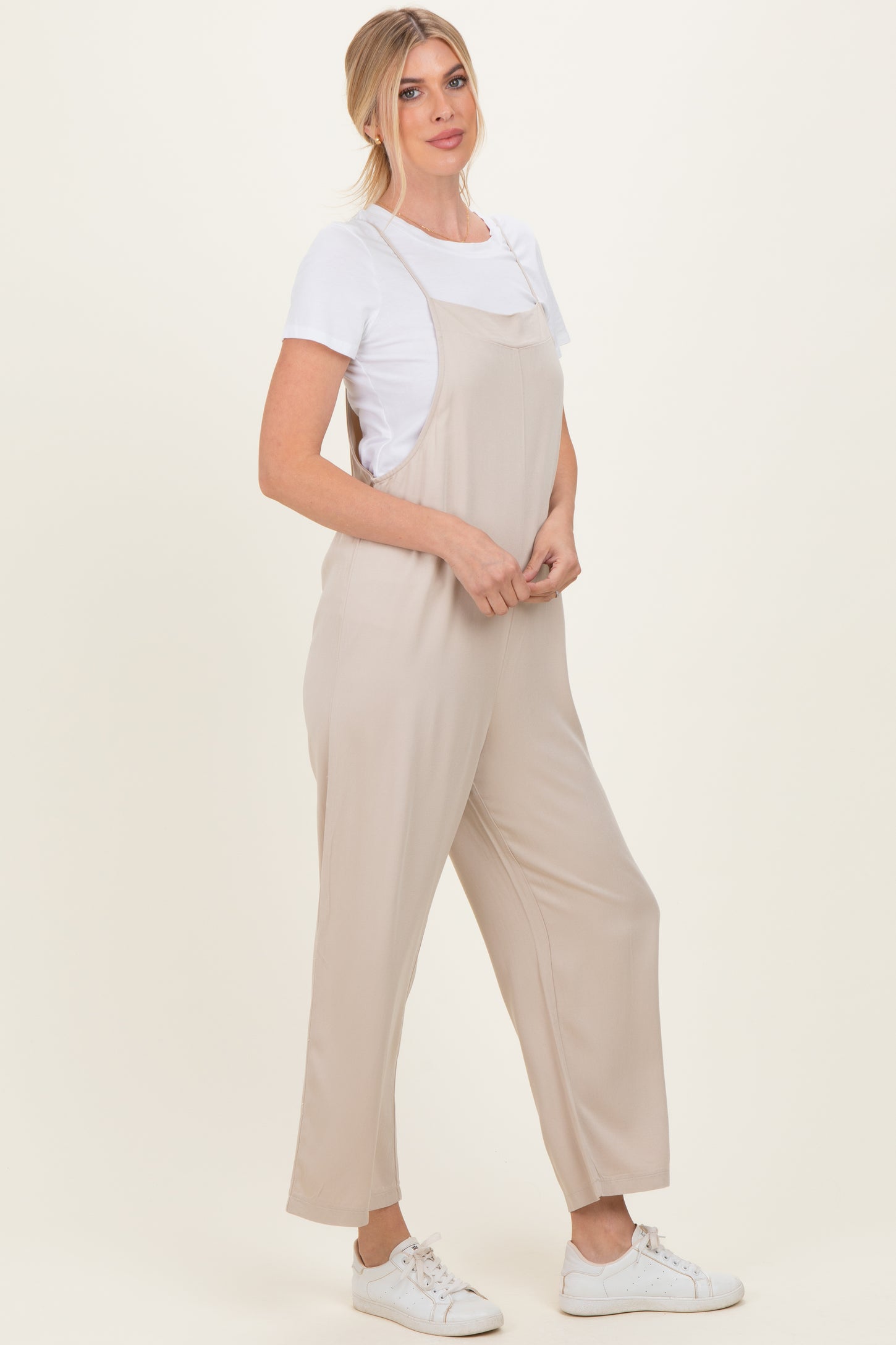 woman wearing a beige sleeveless jumpsuit over a white t-shirt and white sneakers