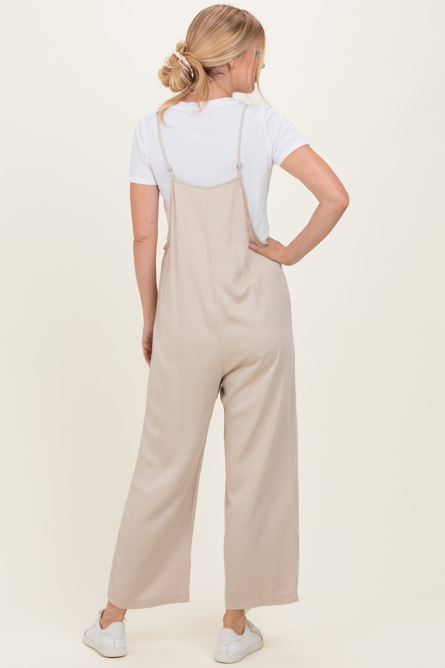 woman wearing a light beige wide-leg jumpsuit with adjustable straps and a white t-shirt underneath