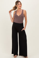 woman wearing a brown ribbed maternity tank top and black wide-leg pants, posing with one hand on her hip