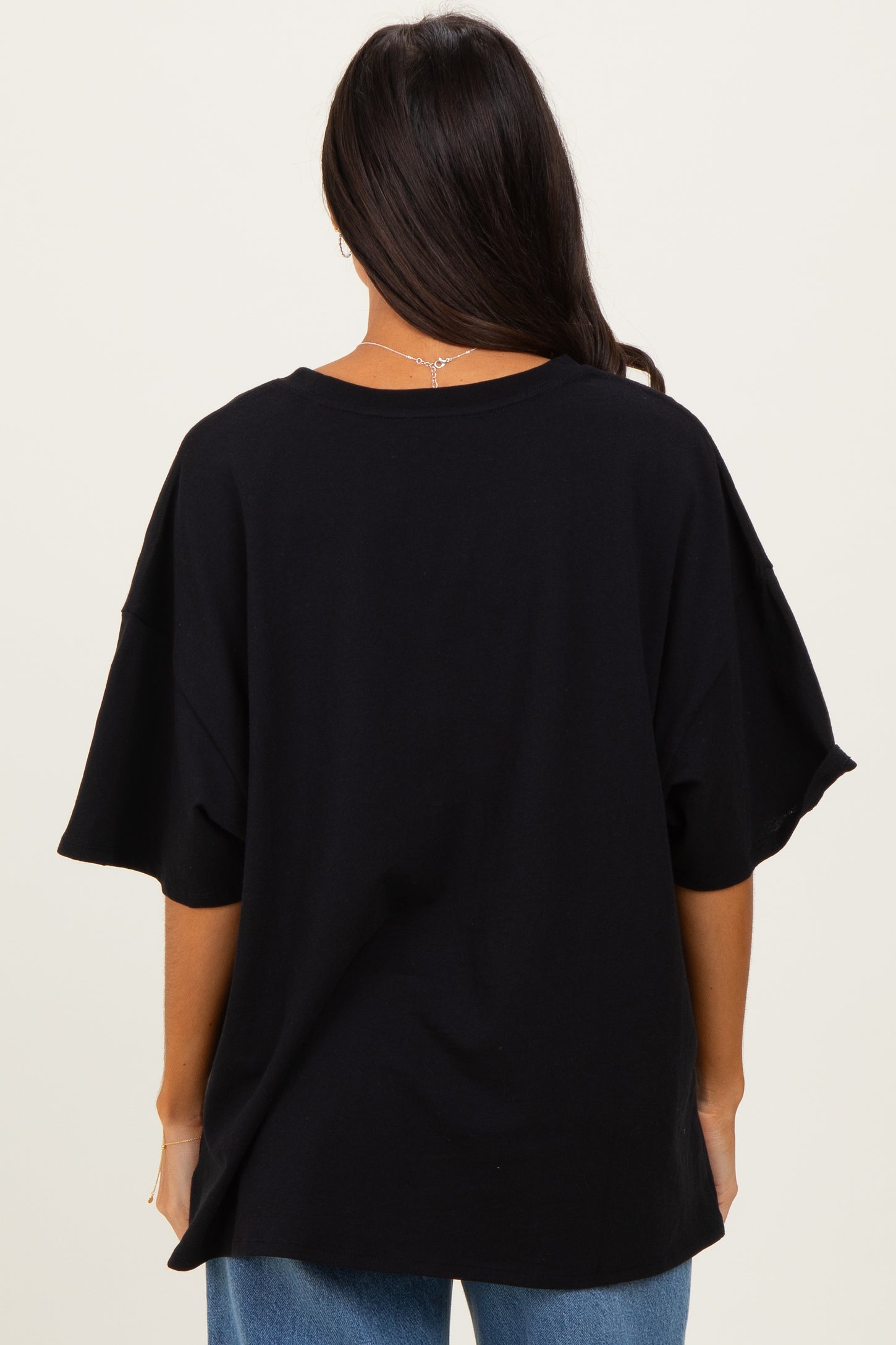 woman wearing a loose-fitting black oversized t-shirt seen from the back, paired with blue jeans