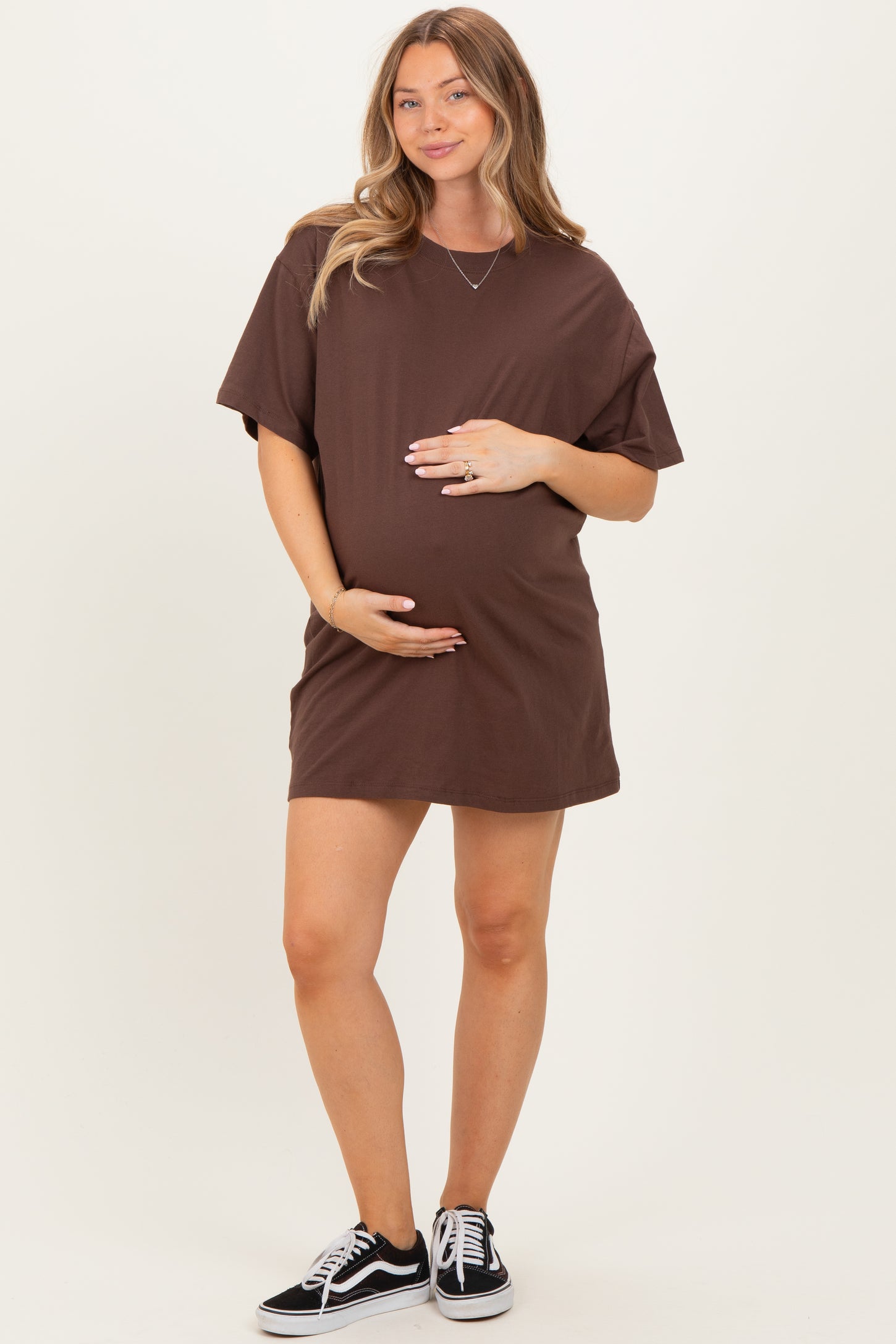 woman wearing a brown oversized t-shirt dress and holding her baby bump, styled with sneakers