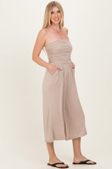 woman wearing a beige strapless jumpsuit with a ruching detail and pockets, styled with black sandals