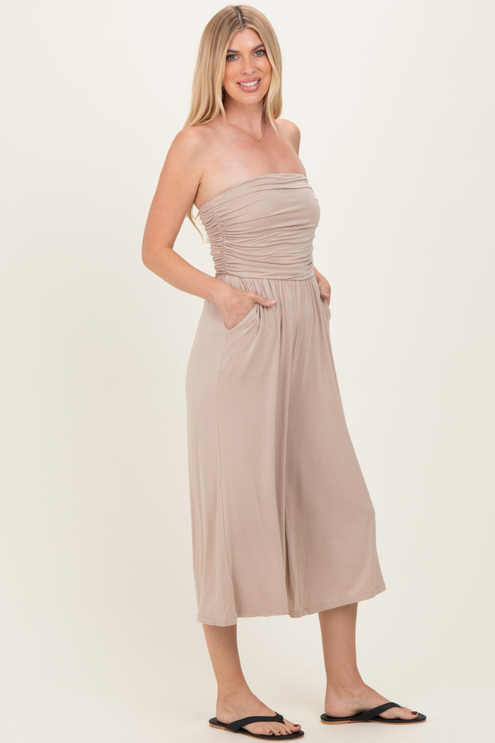woman wearing a beige strapless jumpsuit with a ruching detail and pockets, styled with black sandals