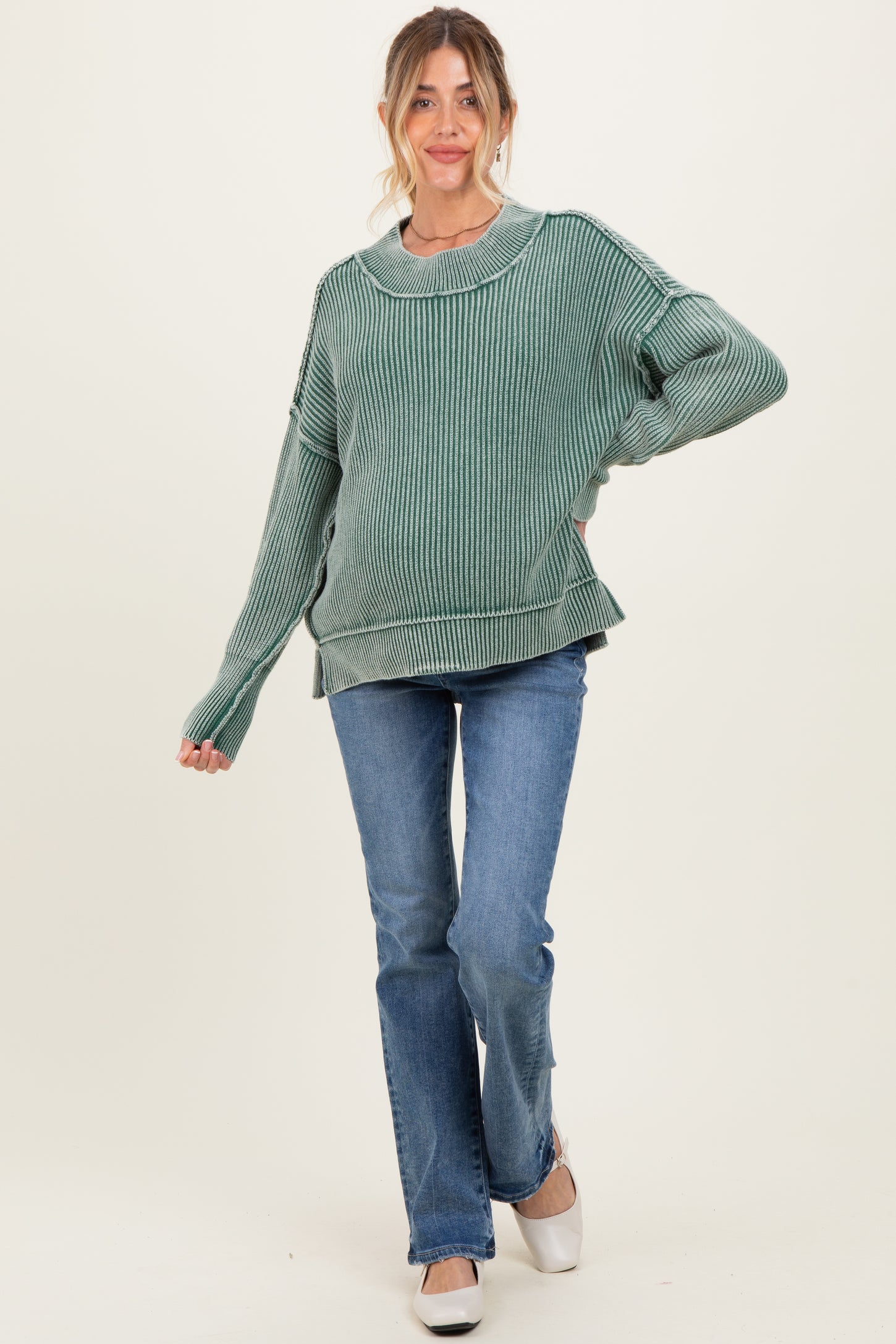 woman wearing a green ribbed maternity sweater and blue jeans, with a relaxed fit and wide sleeves, smiling at the camera