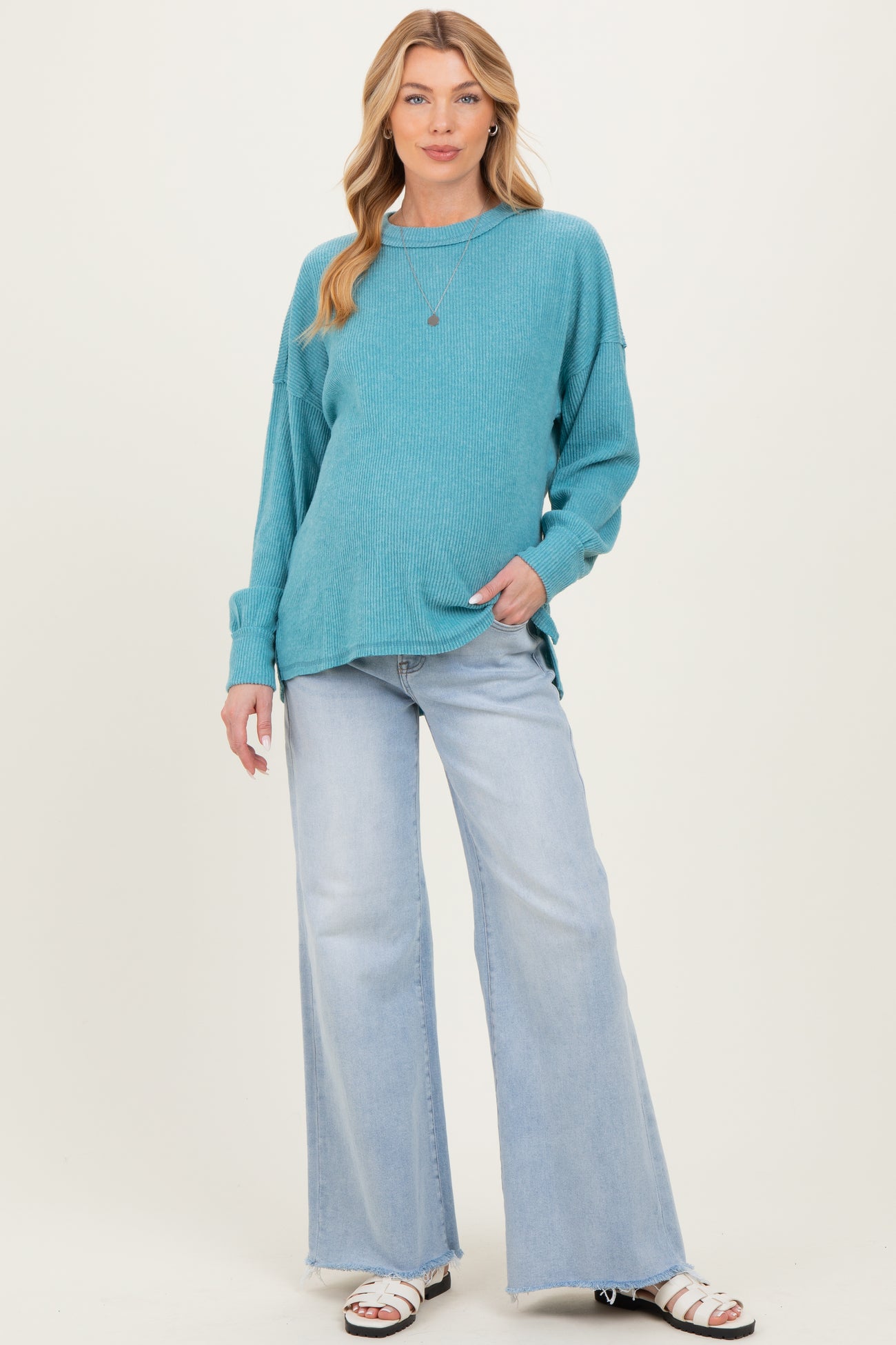 woman wearing a teal maternity sweater with long sleeves and relaxed fit paired with light wash flared jeans