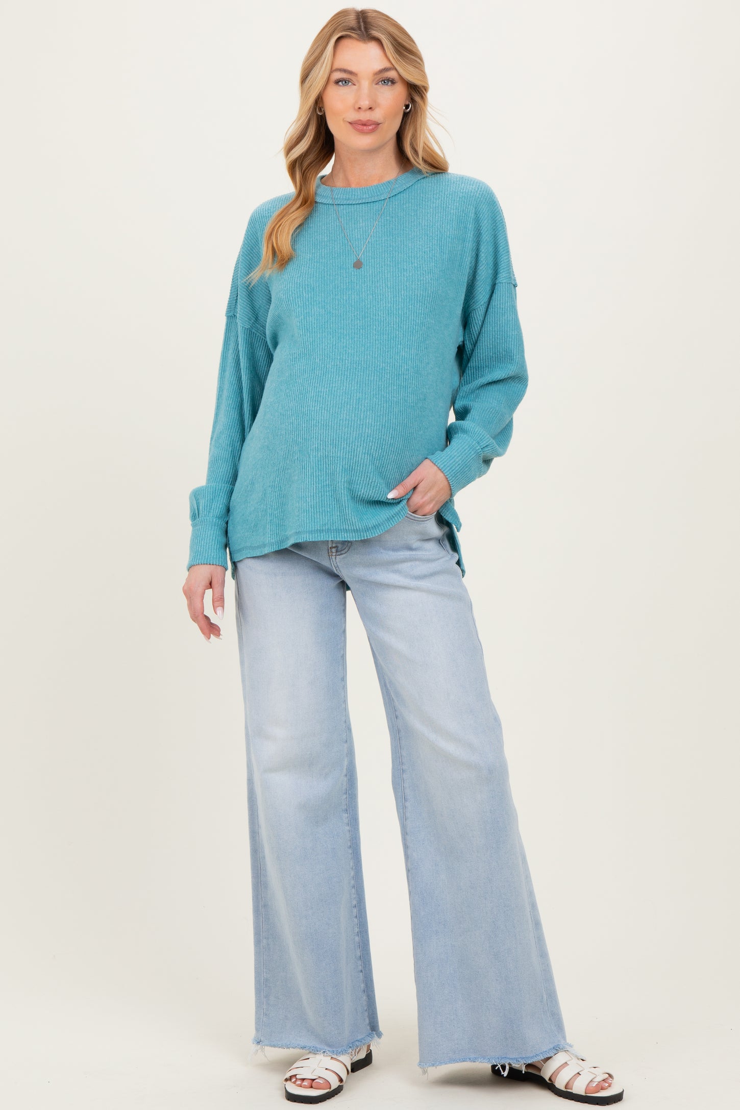 woman wearing a teal maternity sweater with long sleeves and relaxed fit paired with light wash flared jeans