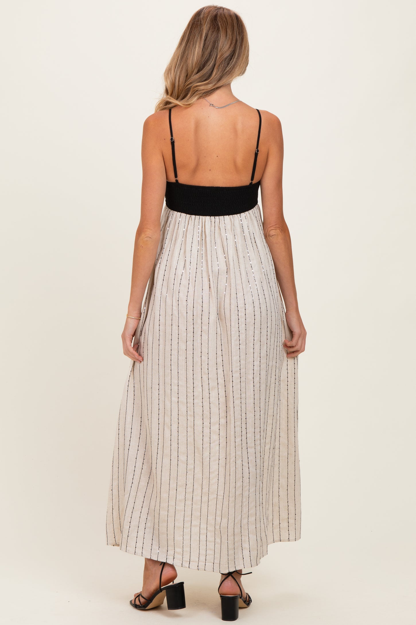 woman wearing a back view of a black and white striped maternity maxi dress with adjustable spaghetti straps
