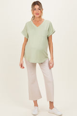 woman wearing a light green v-neck maternity top with a pocket and light beige wide-leg pants, showing her baby bump