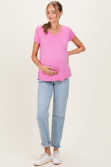 woman wearing a pink short sleeve maternity top and holding her baby bump, paired with light blue jeans
