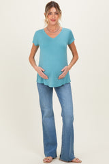 woman wearing a teal short sleeve maternity top and holding her baby bump, paired with flared jeans