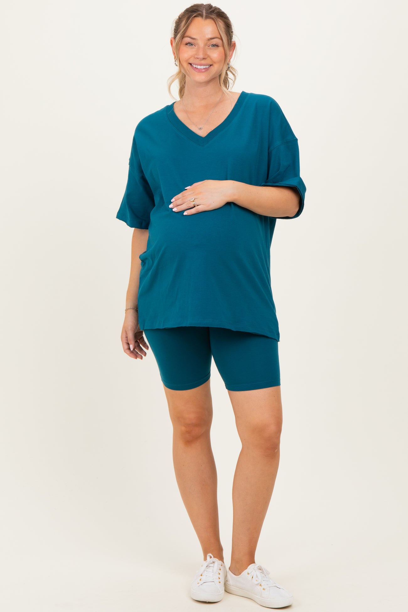 woman wearing a teal maternity t-shirt and matching bike shorts, gently holding her baby bump