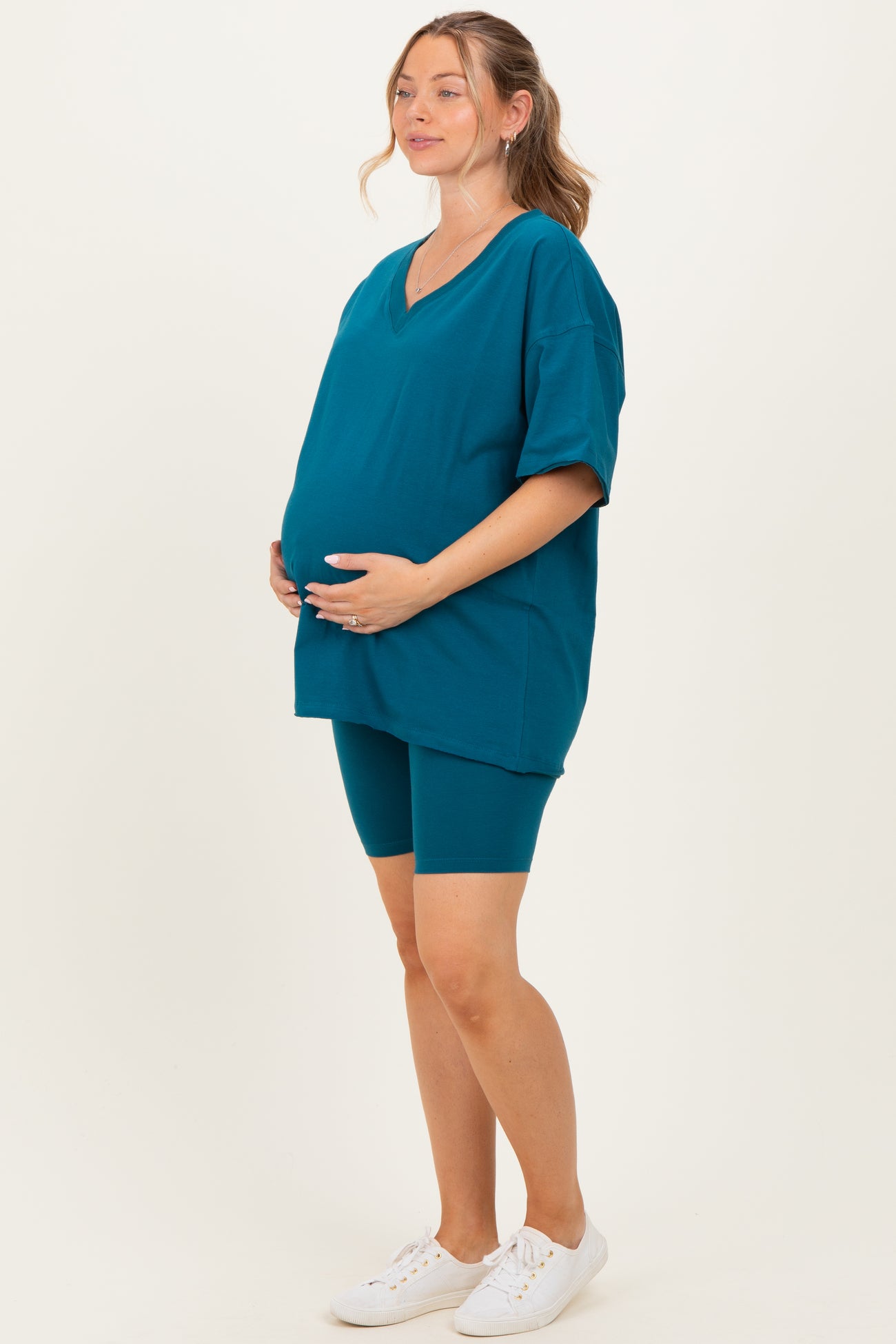woman wearing a teal maternity oversized t-shirt and matching bike shorts, holding her baby bump
