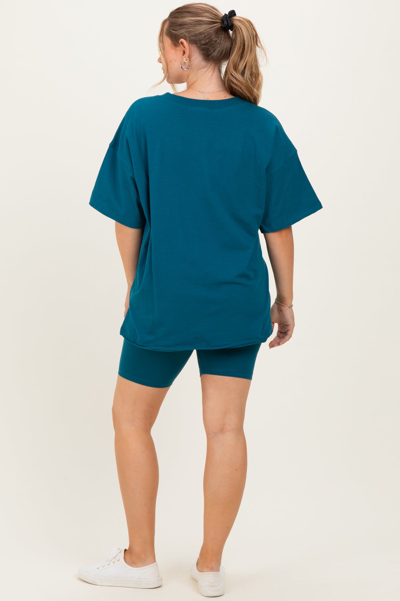 woman wearing a teal oversized maternity t-shirt and matching bike shorts, showing off her baby bump from behind