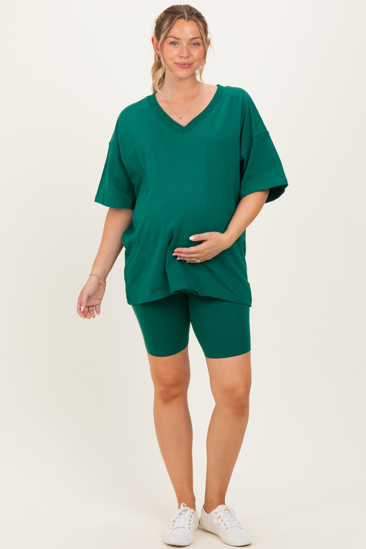 woman wearing a green maternity oversized t-shirt and matching bike shorts, holding her baby bump