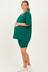 woman wearing a dark green maternity oversized top and matching bike shorts, showing her baby bump