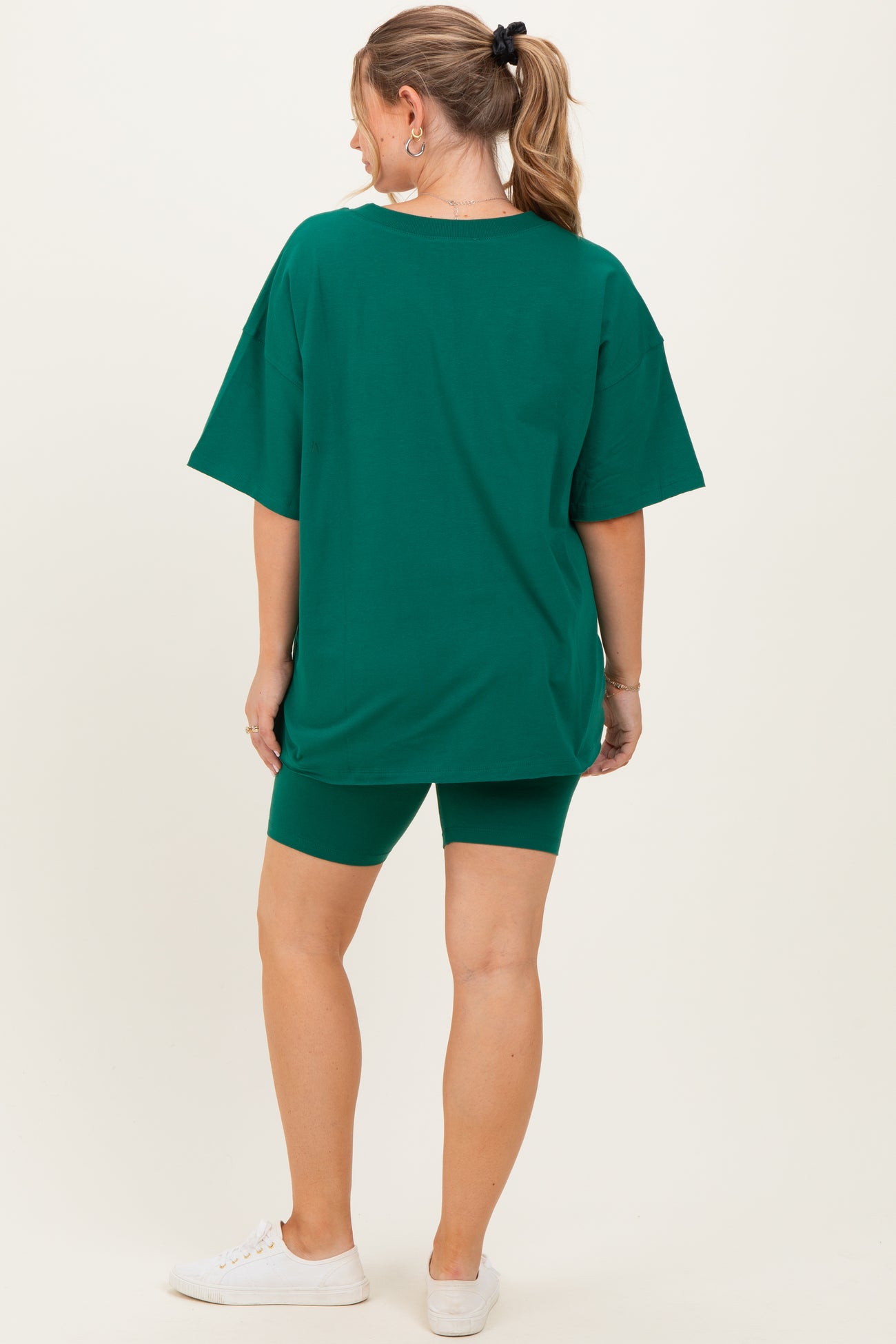 woman wearing a green oversized t-shirt and green biker shorts as maternity wear, showing her baby bump from the back