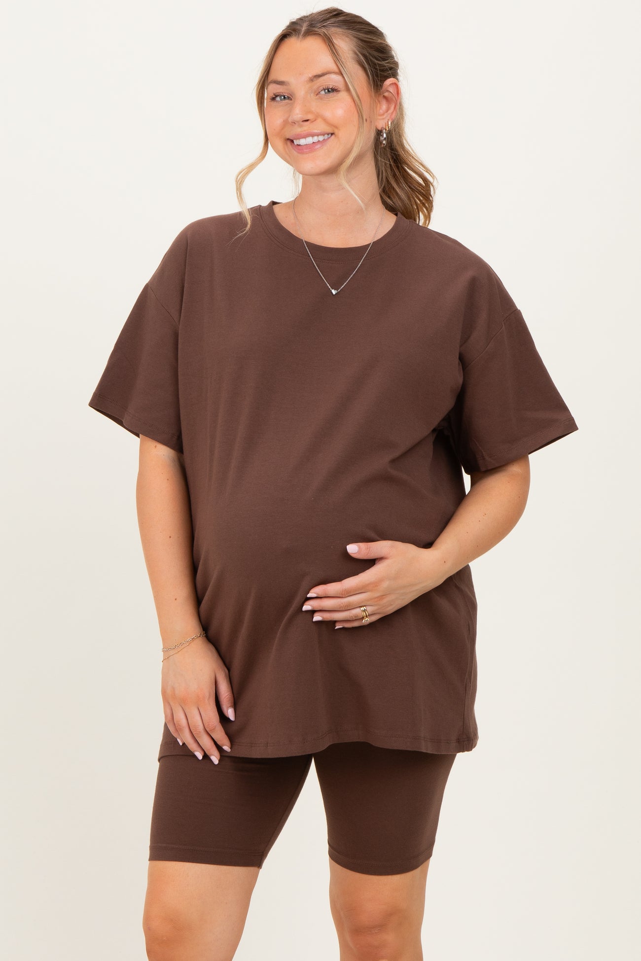 woman wearing a brown oversized maternity t-shirt and matching bike shorts, holding her baby bump