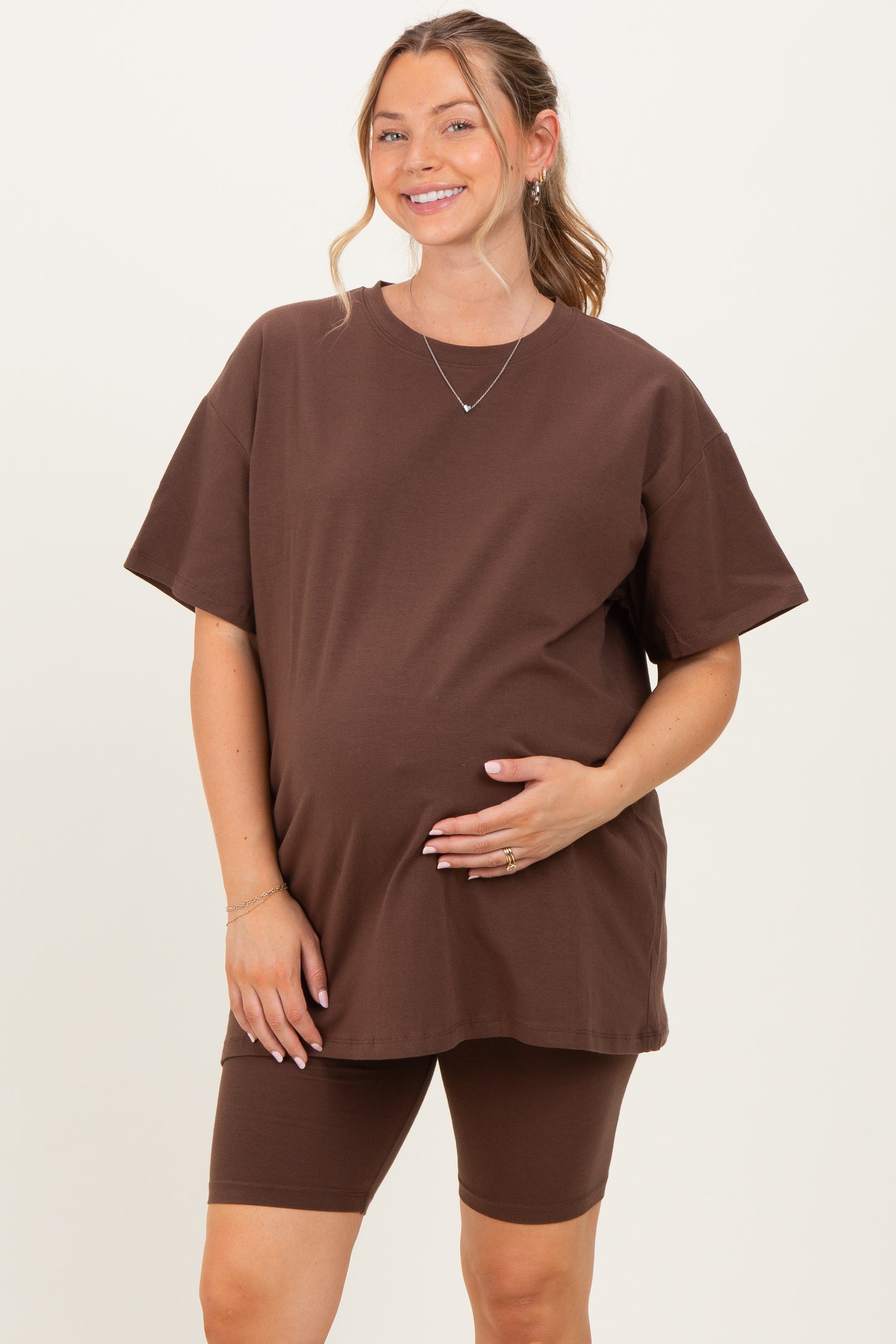 woman wearing a brown oversized maternity t-shirt and matching bike shorts, holding her baby bump