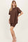 woman wearing a brown oversized t-shirt and matching knee-length shorts, standing barefoot against a light background