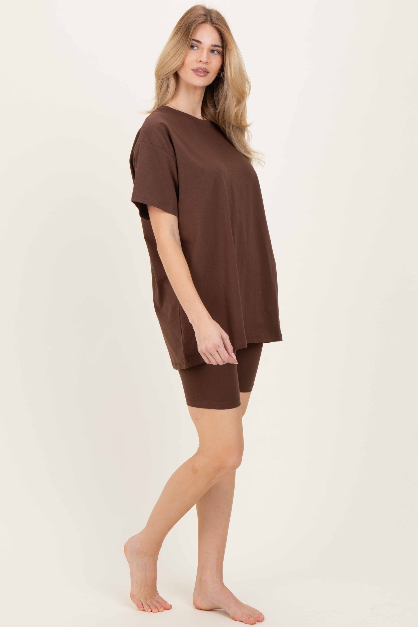 woman wearing a brown oversized t-shirt and brown biker shorts, standing barefoot, styled casually