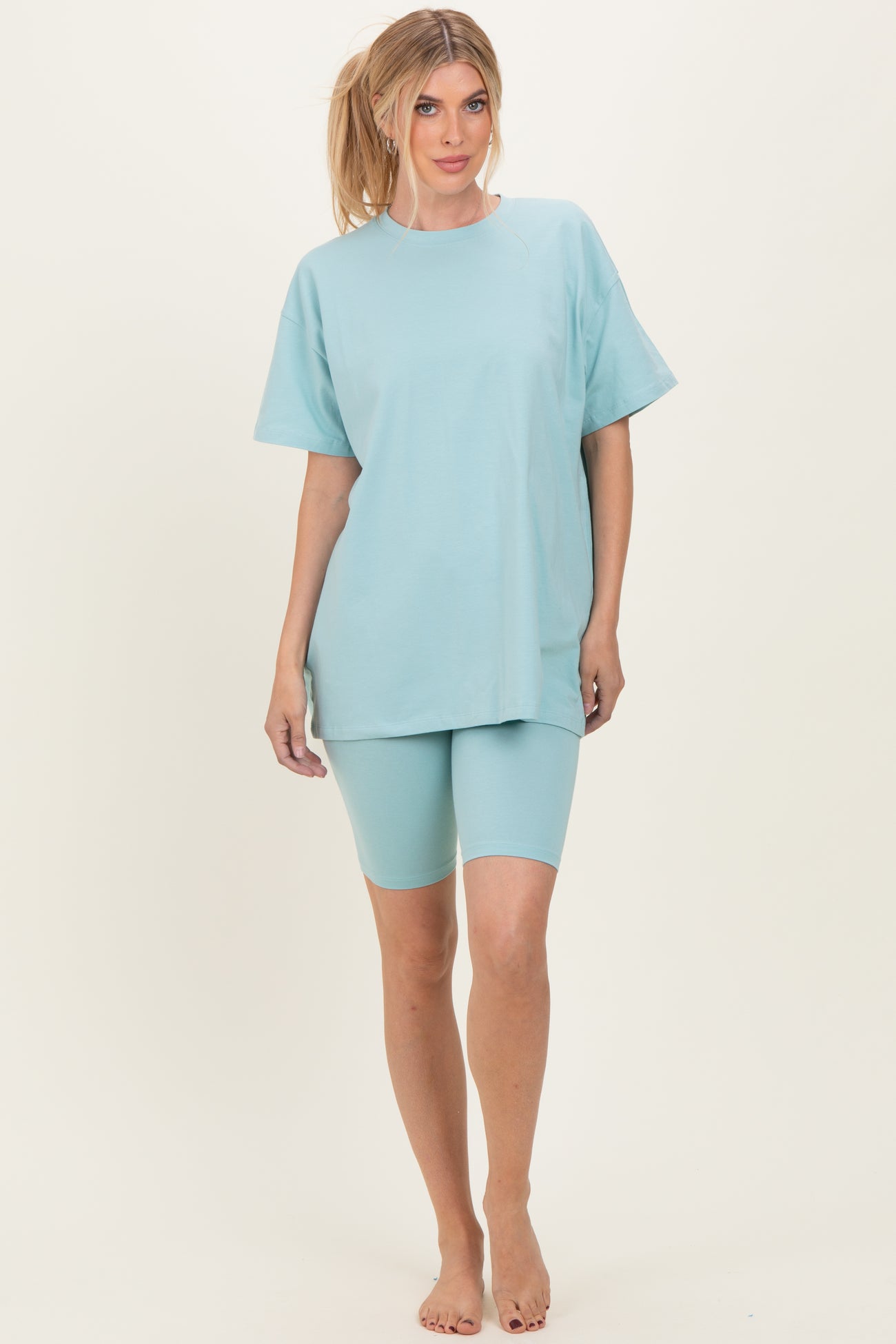 woman wearing a light blue oversized t-shirt and matching bike shorts, standing barefoot on a neutral background
